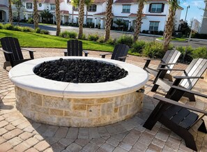 A circular stone fire pit with seating around it, set on a paved patio.