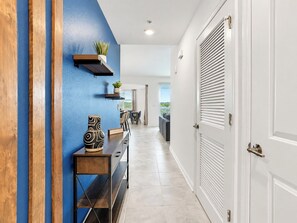 Un couloir avec un mur bleu, un banc en bois, une console ornée d’objets décoratifs et une porte avec un volet.