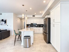 A modern kitchen with white cabinetry, a stainless steel refrigerator, and a central island with bar stools.
