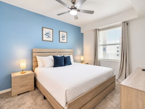 A bedroom with a bed, bedside tables, a ceiling fan, and a window with curtains.