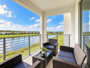 A balcony with wicker furniture and a view of a lake and golf course.