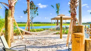 A beach with a hammock, wooden chairs, a wooden structure, and a view of a lake. - Themed Rooms & Lake Views: Your Kissimmee Escape! (Kissimmee)