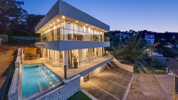 A modern two-story house with a swimming pool, large windows, and a balcony.