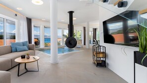 Ein modernes Wohnzimmer mit großem Fenster, Kamin, Pool und Fernseher.