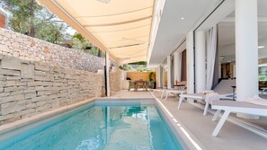 A poolside area with a stone wall, lounge chairs, and a covered seating area.