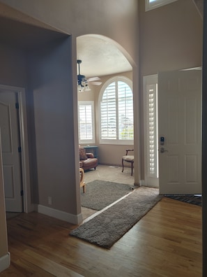 A spacious living room with a high ceiling, a large arched window, and a wooden floor.