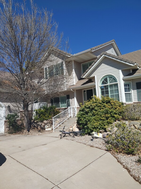 A two-story house with a covered front porch, a stone foundation, and a large tree in the front yard.