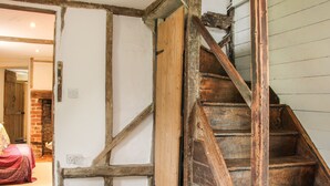 A wooden staircase with a rustic design, leading to a room with a brick fireplace and a bed with a red blanket. - Denbigh Hall (Leominster)