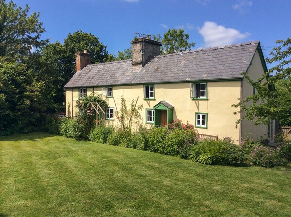Une maison à deux étages avec une porte verte, de nombreuses fenêtres et une cheminée.