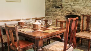 A dining room with a wooden table set for six, surrounded by chairs with patterned cushions. A stone wall and fireplace are visible in the background. - Denbigh Hall (Leominster)