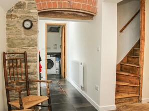 Un couloir étroit avec un mur en pierre, une chaise en bois, un lave-linge et un escalier.