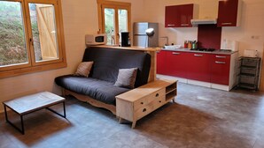 A compact living space with a sofa, a small table, and a kitchenette area with red cabinets and a microwave. - Porticcio house near the sea (Grosseto-Prugna)