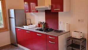 A compact kitchen with red cabinets, a stainless steel refrigerator, a gas stove, and a toaster. - Porticcio house near the sea (Grosseto-Prugna)
