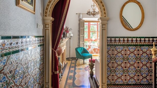 Een hal met sierlijk betegelde vloer, een blauwe fauteuil en een spiegel aan de muur.