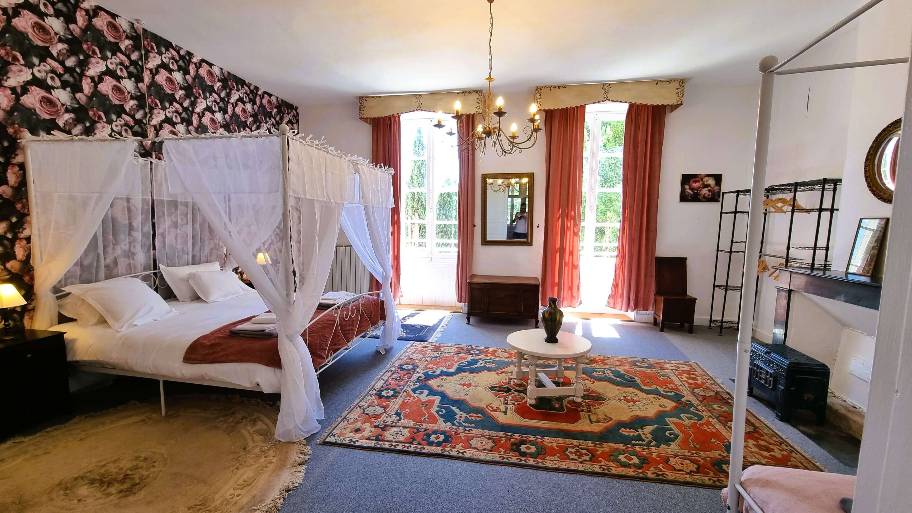 A bedroom with a four-poster bed, a chandelier, a large mirror, and a patterned rug.