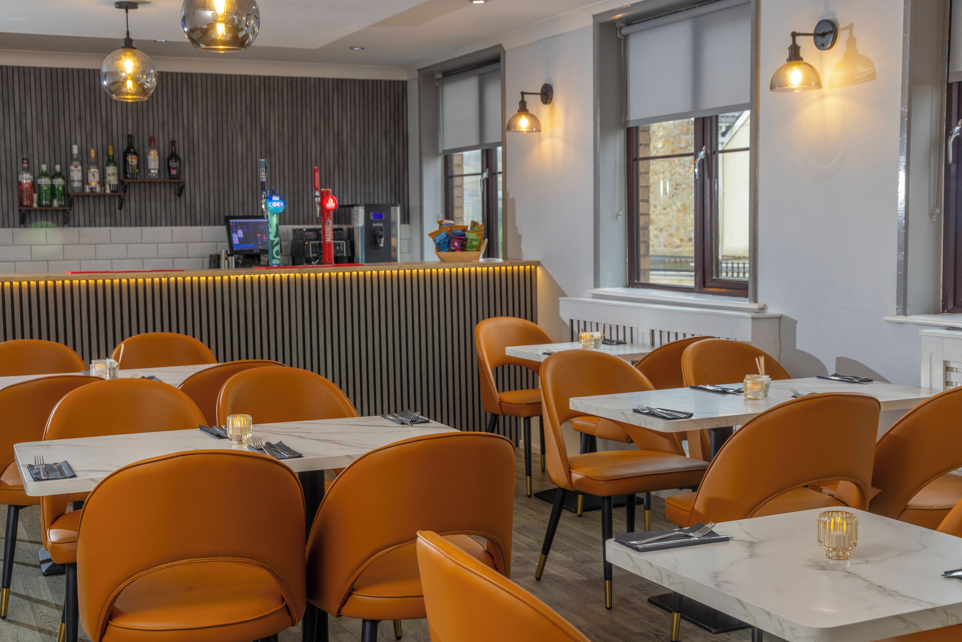 A restaurant with orange chairs, white tables, and a bar area with bottles and a cash register.