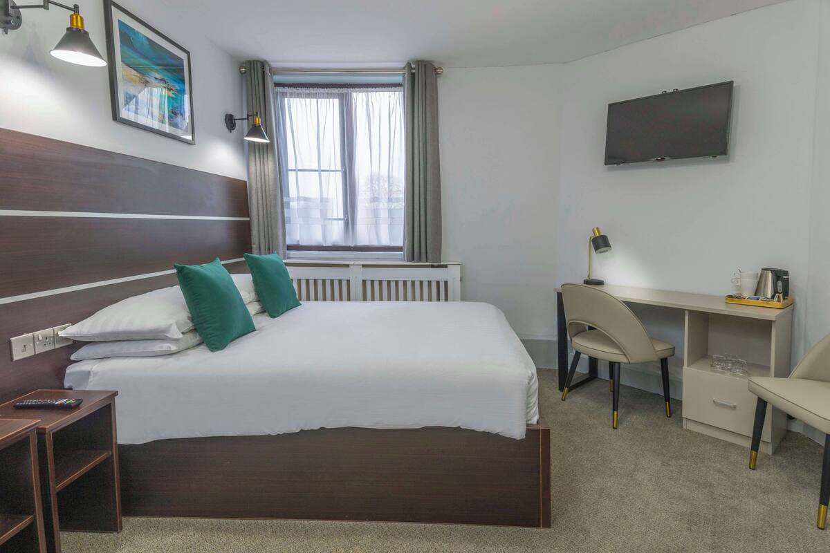 A hotel room with a bed, a desk, a chair, a TV, and a window with curtains.