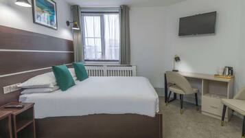 Ein Hotelzimmer mit Bett, Schreibtisch, Sessel, Fernseher und einem Fenster mit Vorhängen.