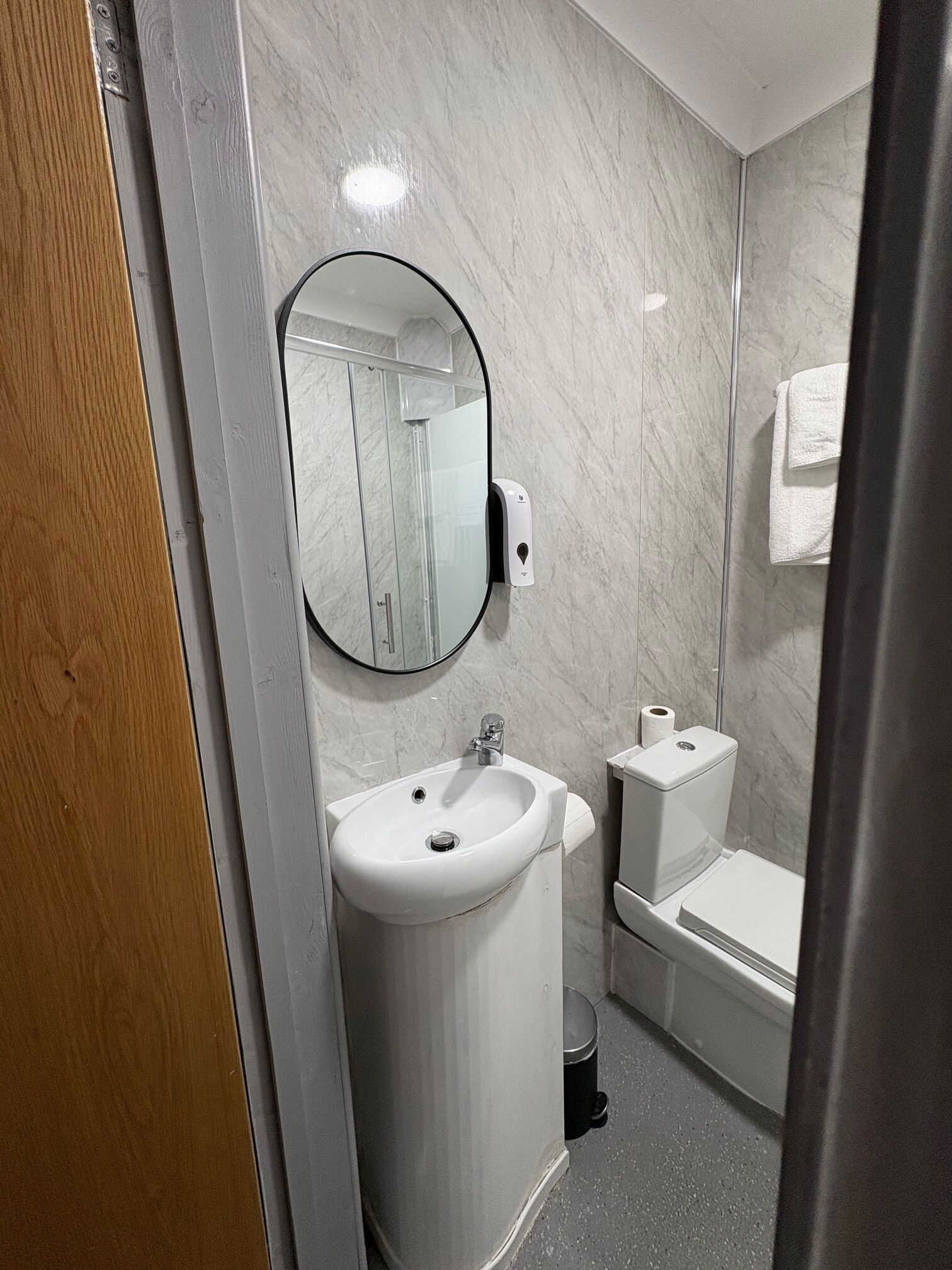 Une salle de bain moderne avec un mur en marbre, un miroir rond, un lavabo, des toilettes et une douche.