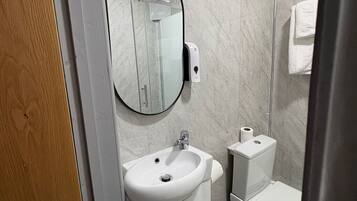 Une salle de bain moderne avec un mur en marbre, un miroir rond, un lavabo, des toilettes et une douche.