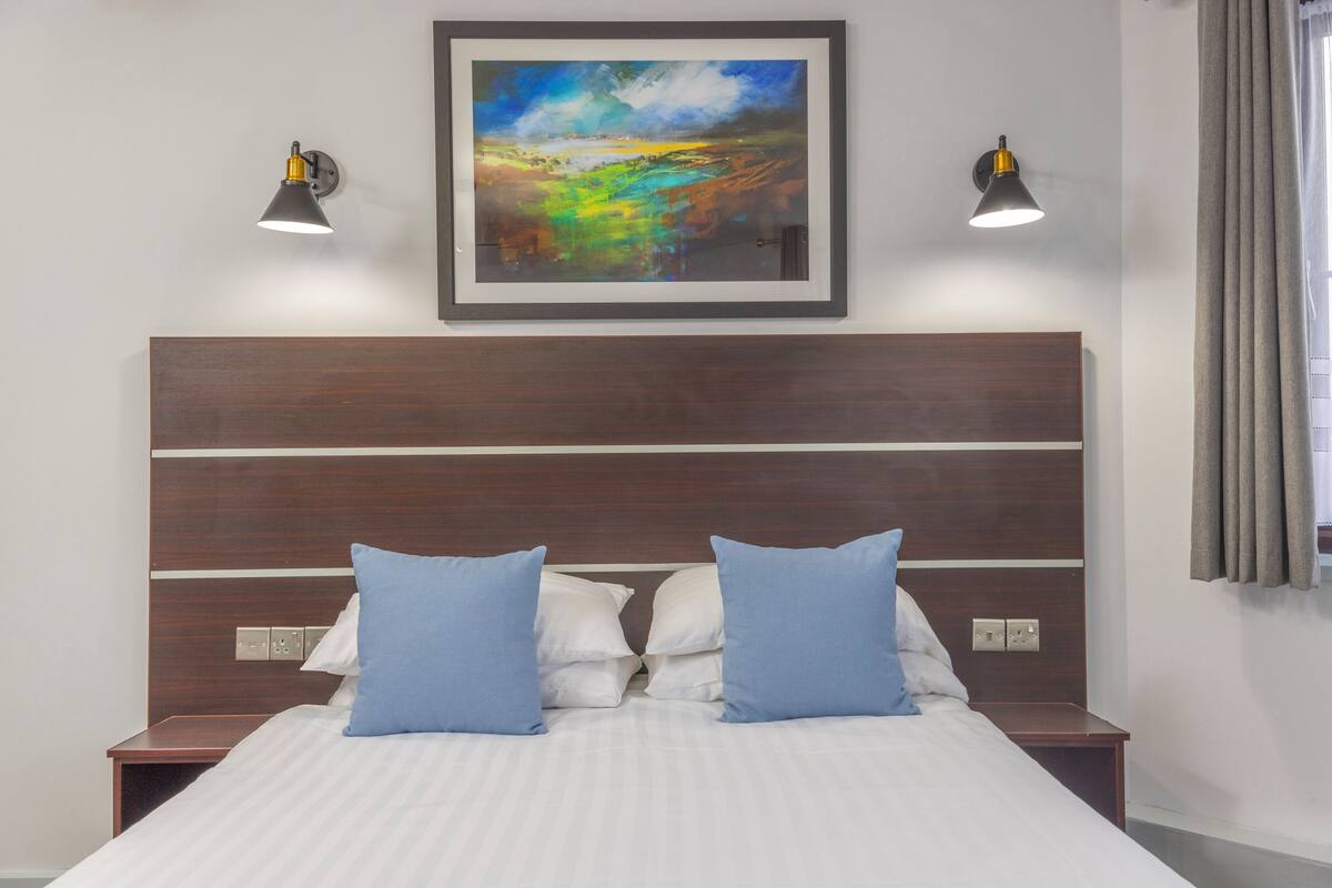 A neatly made bed with blue pillows, a wooden headboard, and two wall-mounted lamps.