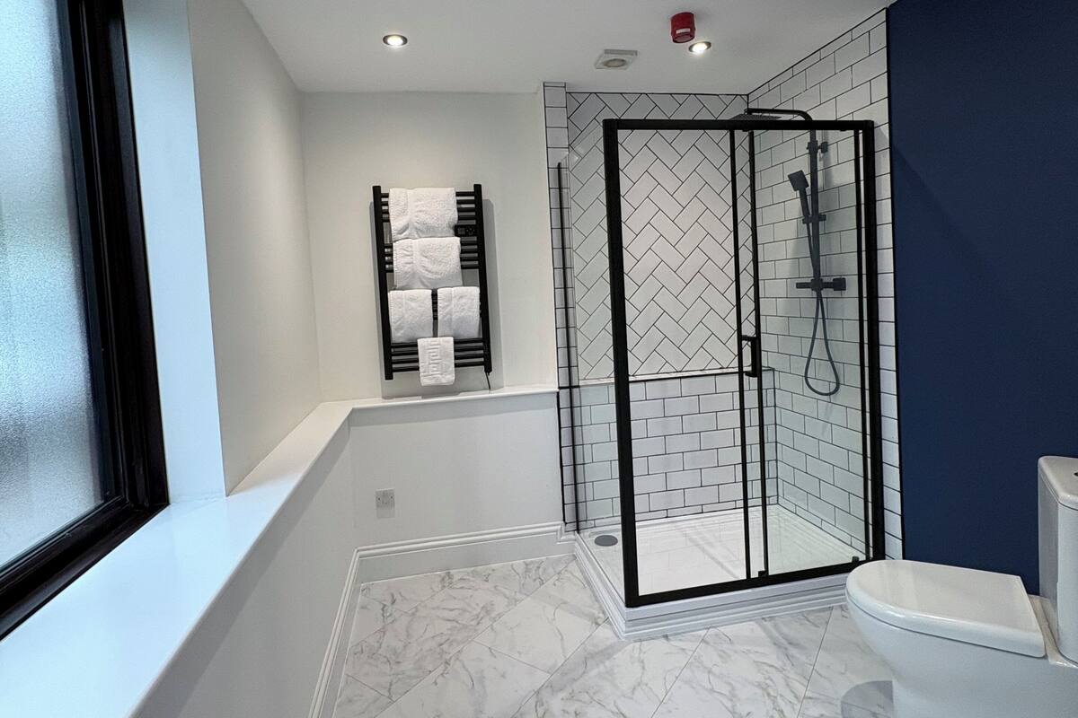A modern bathroom with a glass-enclosed shower, a white toilet, and a bathtub with a towel rack.