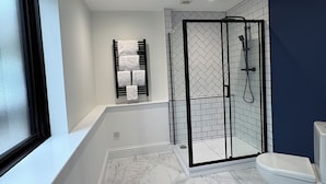A modern bathroom with a glass-enclosed shower, a white toilet, and a bathtub with a towel rack.