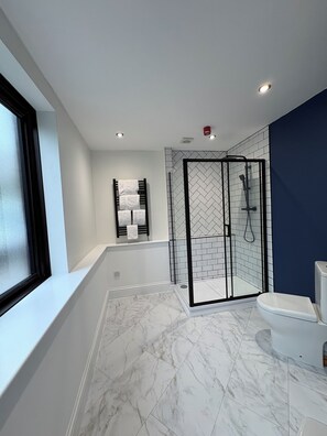 A modern bathroom with a glass-enclosed shower, a white toilet, and a bathtub with a towel rack.