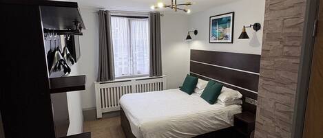 A modern bedroom with a large bed, a built-in wardrobe, a radiator, and a window with curtains.