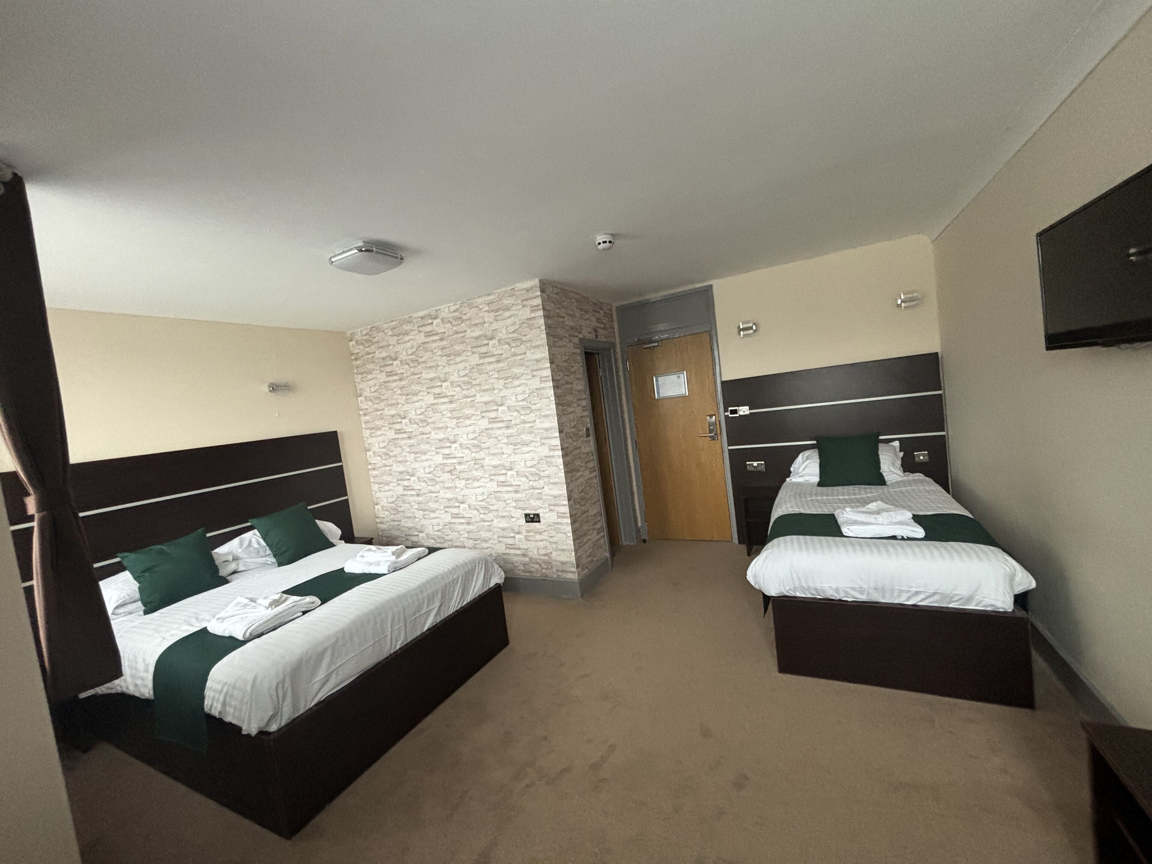 Habitación de hotel con dos camas, una pared de acento de piedra, una puerta de madera y un televisor de pantalla plana en la pared.