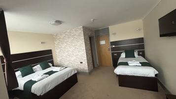 A hotel room with two beds, a stone accent wall, a wooden door, and a flat-screen TV on the wall.