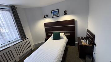 A neatly arranged hotel room with a single bed, a bedside table with a lamp, a small picture on the wall, and a radiator.
