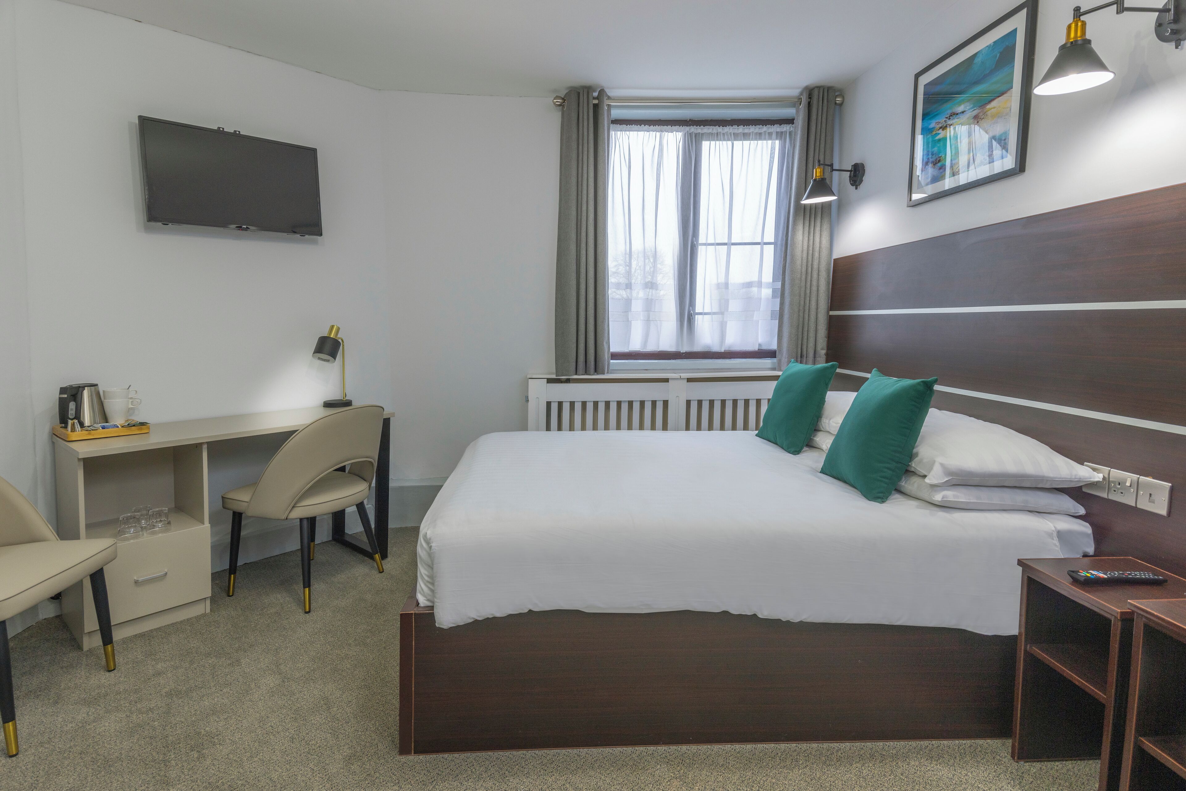 A hotel room with a bed, desk, chair, TV, window, and artwork on the wall.