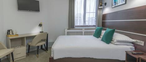 A hotel room with a bed, desk, chair, TV, window, and artwork on the wall.