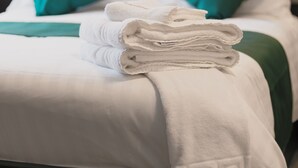 A neatly made bed with white linens, green pillows, and a folded white towel on the bed.
