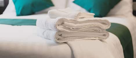 Un lit bien fait, avec des draps blancs, des coussins verts et une serviette blanche pliée posée sur le lit.