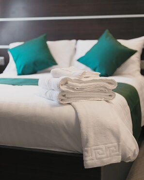 A neatly made bed with white linens, green pillows, and a folded white towel on the bed.