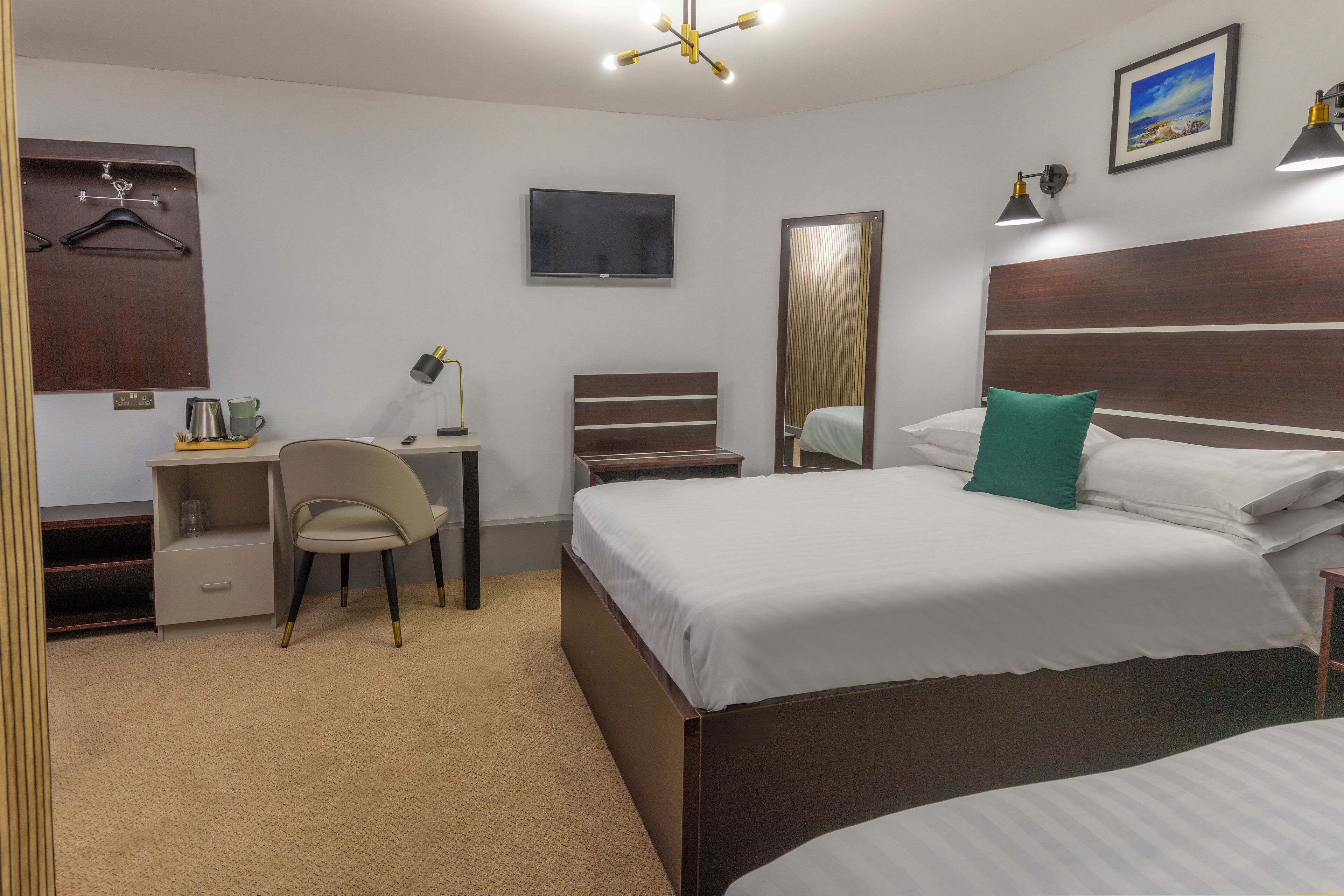 A hotel room with a bed, a desk with a chair, a TV, a mirror, and a nightstand.