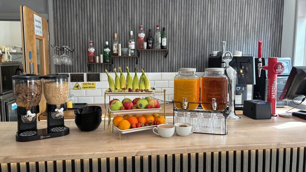 A kitchen counter with a coffee machine, a fruit display, and a beverage dispenser. - Best Western Ebbw Vale (Ebbw Vale)