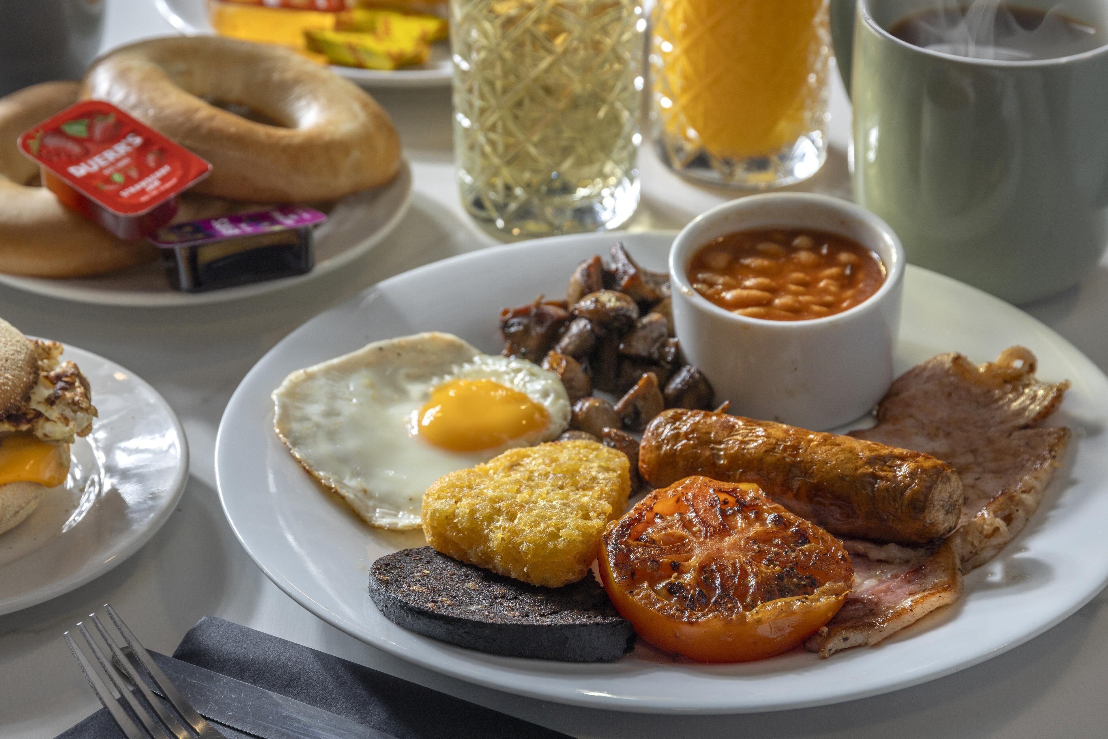 Une assiette de petit-déjeuner comprenant des œufs, des saucisses, des haricots et une tomate grillée.