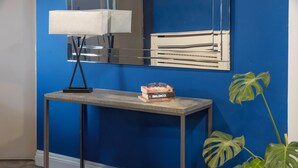 A modern room with a blue wall, a grey console table, a lamp, a stack of books, and a large green plant. - Best Western Ebbw Vale (Ebbw Vale)