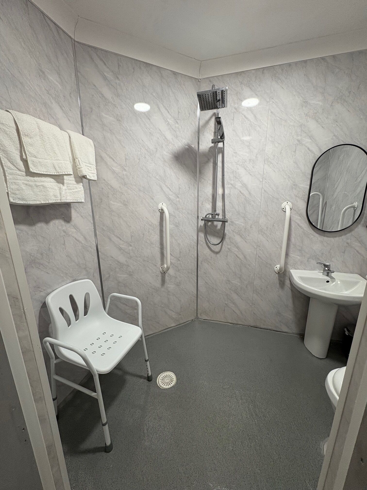 A modern bathroom with a shower, a sink, a mirror, and a wheelchair-accessible chair.