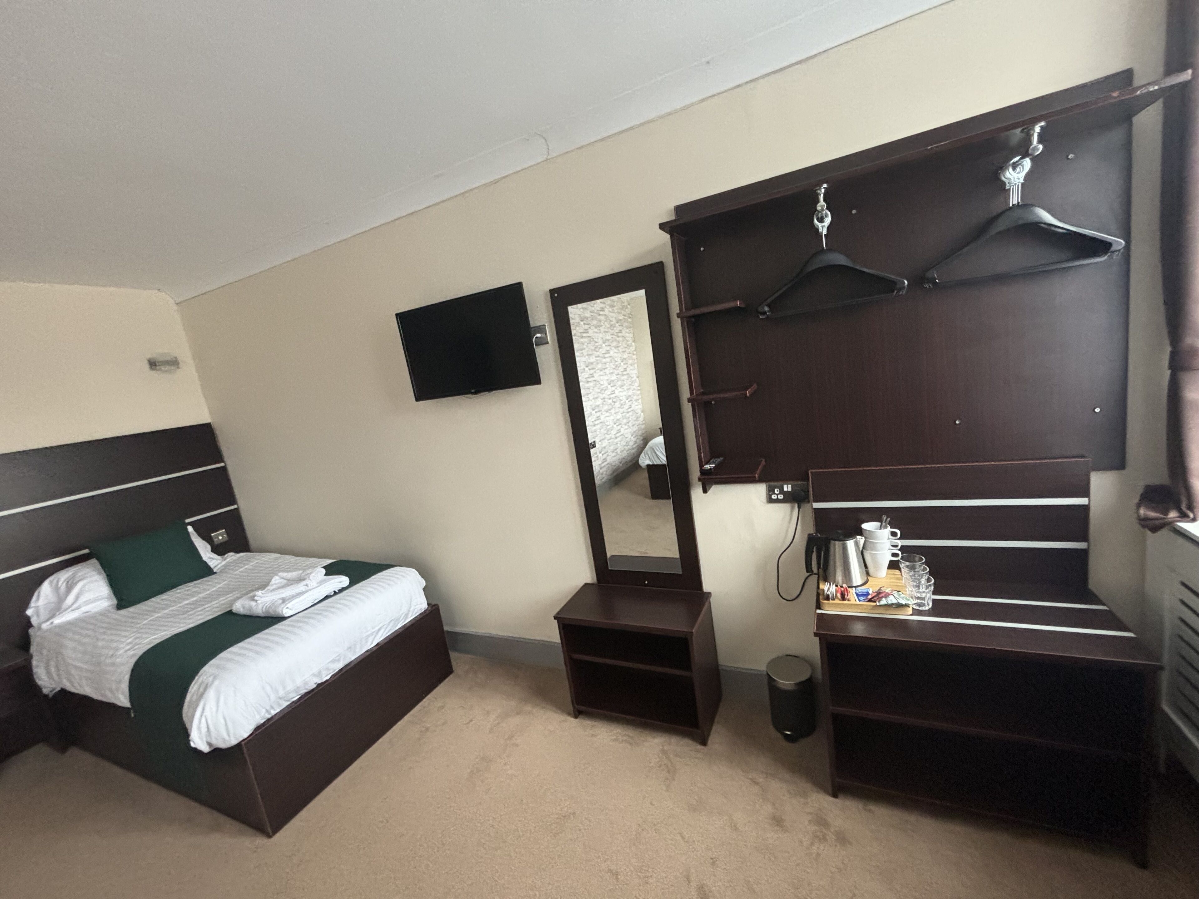 A hotel room with a bed, a dresser, a mirror, a TV, and a coat rack.