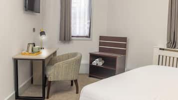 A hotel room with a bed, a desk with a lamp, a chair, a TV mounted on the wall, and a window with curtains.