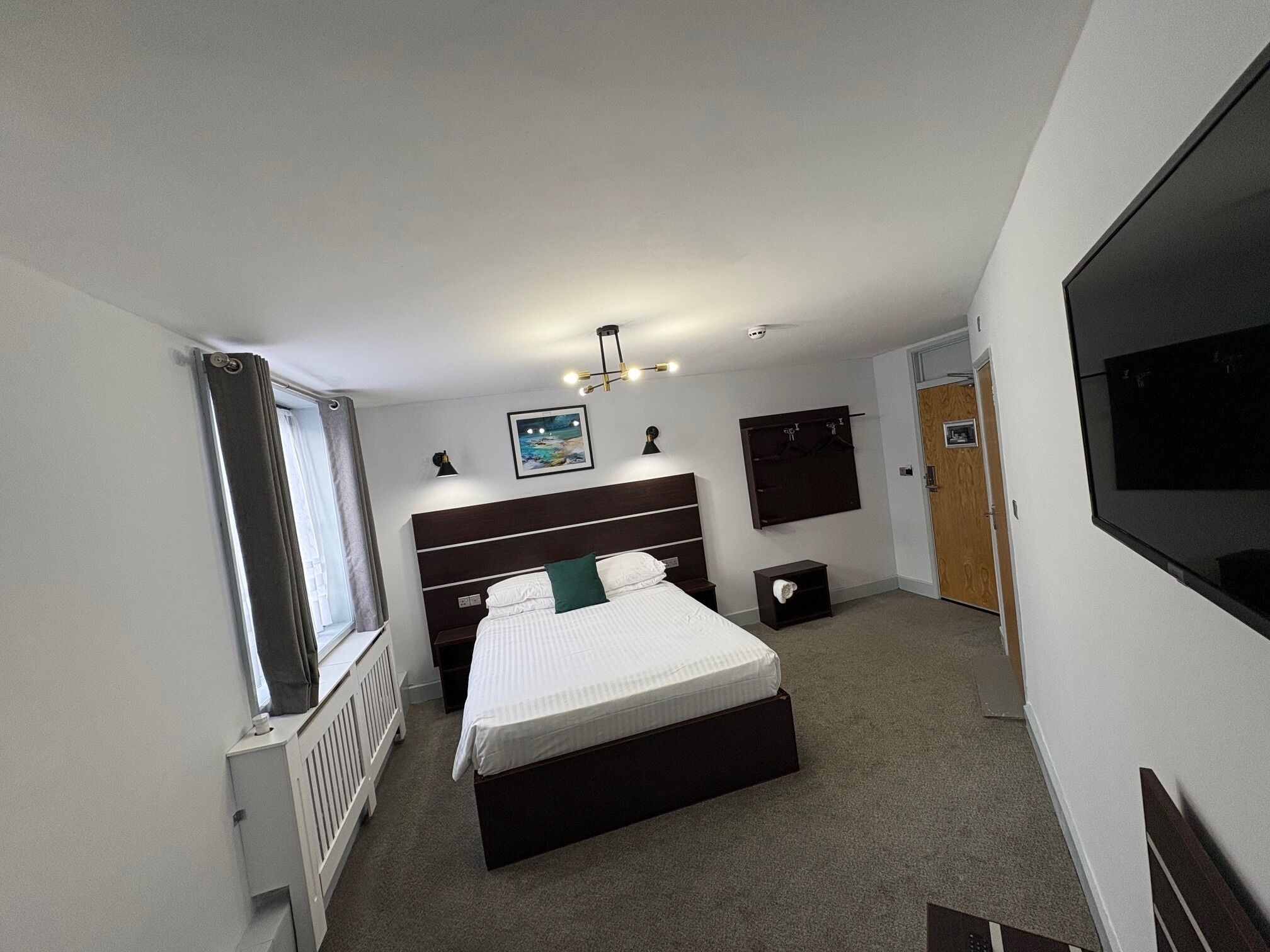 A bedroom with a bed, a bedside table, a dresser, a mirror, and a television.
