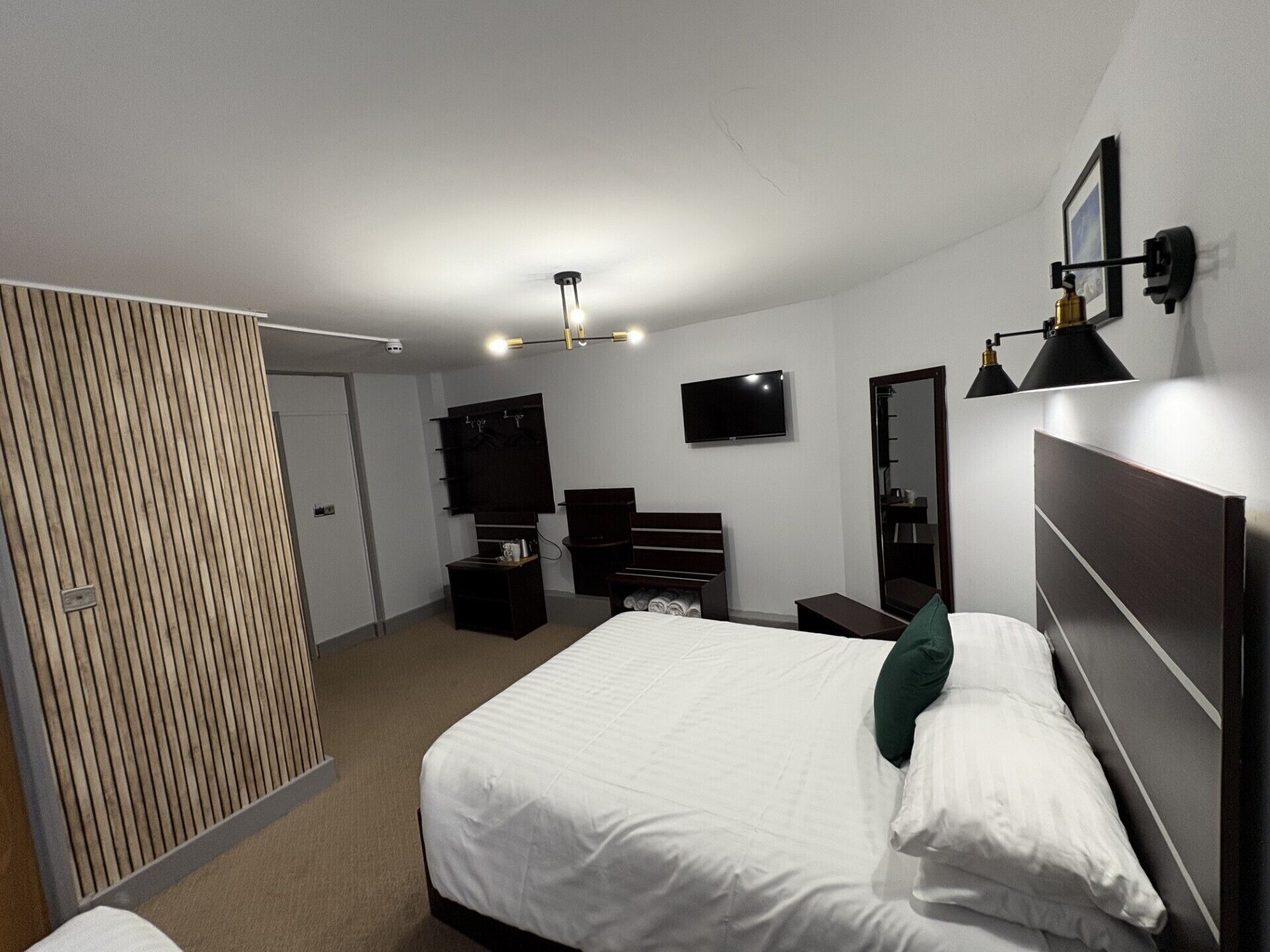 Ein modernes Hotelzimmer mit einem großen Bett, einem Fernseher, einem Schreibtisch und einem Kleiderschrank.