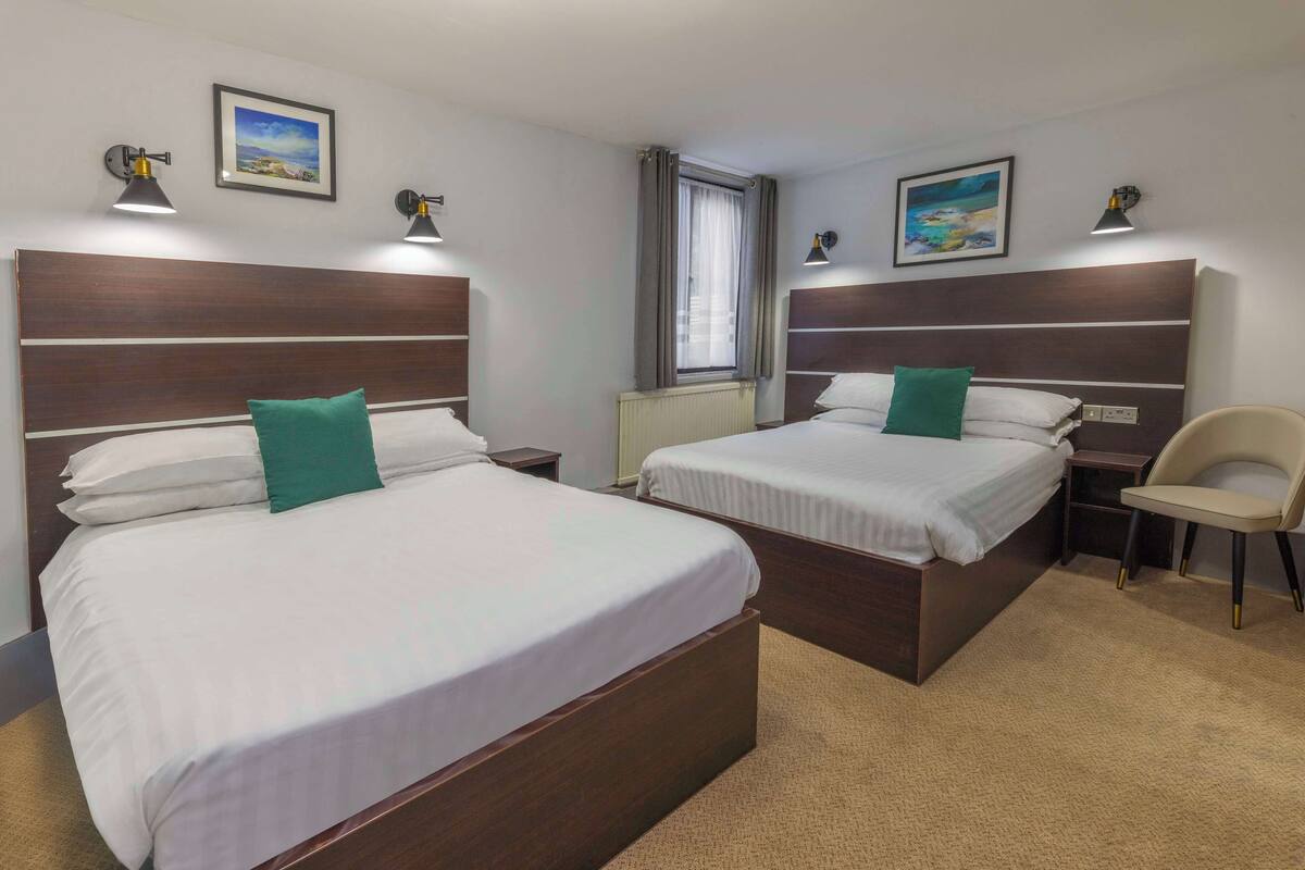 A hotel room with two beds, a chair, and a window with curtains.