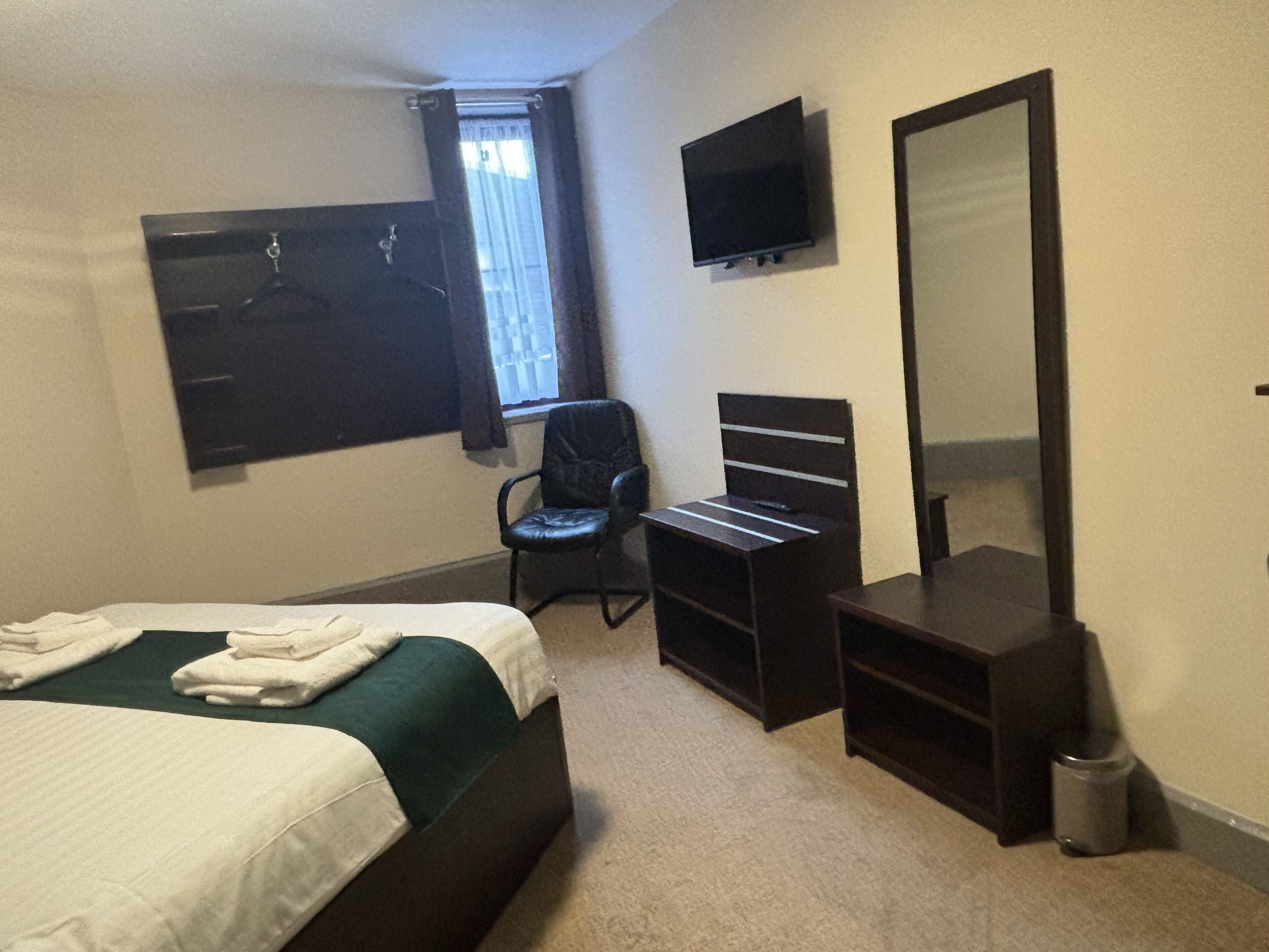 A hotel room with a bed, a desk, a chair, a TV, a mirror, and a window with curtains.
