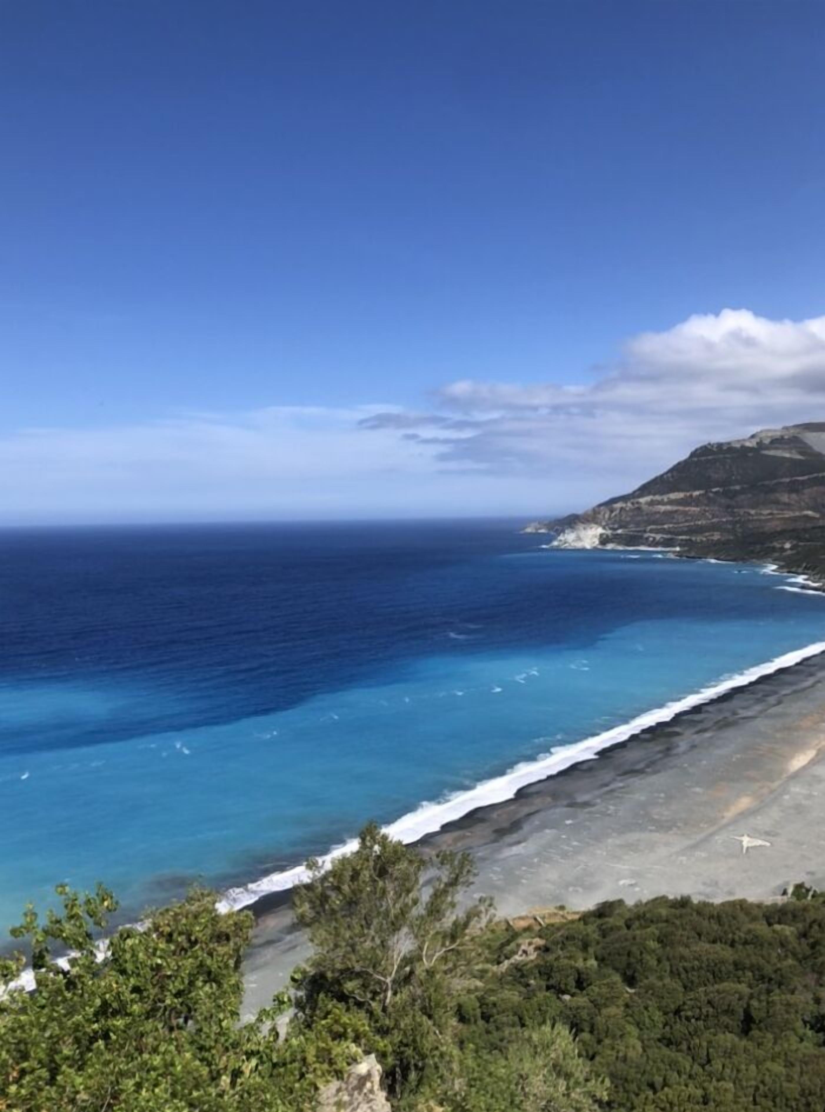 Eine Küstenlandschaft mit freiem Blick auf den Ozean, einem Sandstrand und einem gebirgigen Hintergrund.