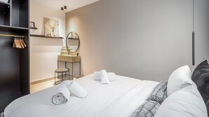 Une chambre d’hôtel moderne avec un lit bien fait, une coiffeuse avec un miroir et une armoire où sont suspendus des vêtements.